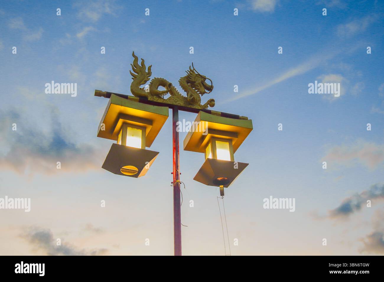 Basso angolo di lanterna dorata del drago che si illumina calorosamente sul pilastro rosso al crepuscolo, con sfondo blu e oro del cielo, elegante design culturale. Foto Stock