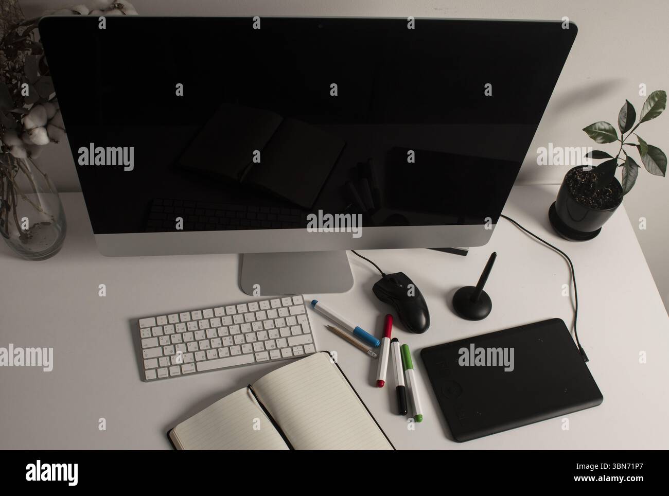 Spazio di lavoro minimalista per l'ufficio domestico con computer desktop, tastiera, notebook, tavoletta grafica, fiori secchi e una pianta su una scrivania bianca pulita. Lavora a casa Foto Stock