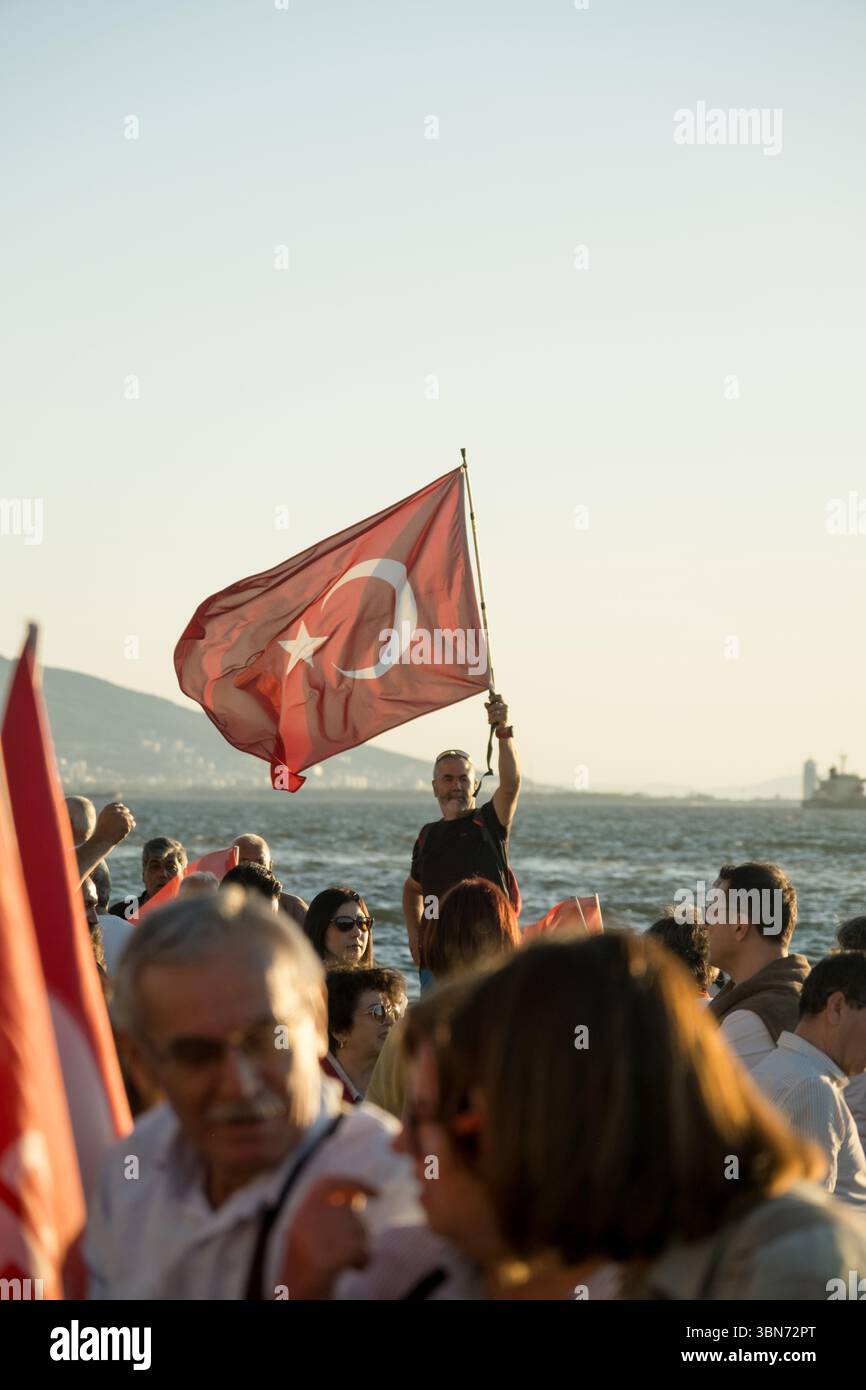 Smirne, Turchia - 19 maggio 2025: L'uomo che regge la bandiera turca si trova in mezzo alla folla con sfondo marino durante le celebrazioni nazionali. Foto Stock