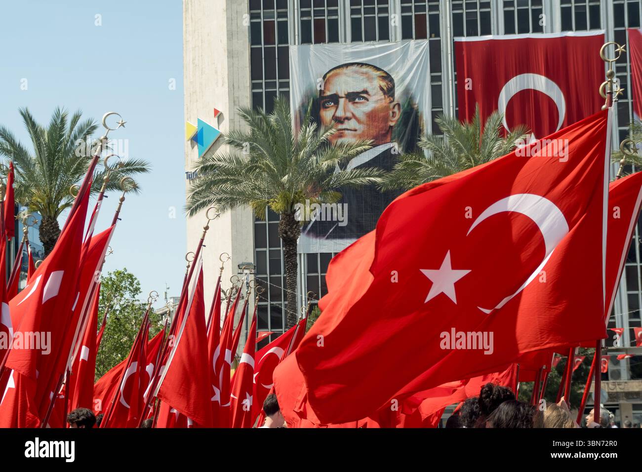 Izmir, Turchia - 19 maggio 2025: Folla che sventola grandi bandiere turche durante la commemorazione Ataturk e la giornata dello sport giovanile con un ritratto gigante di Ataturk Foto Stock