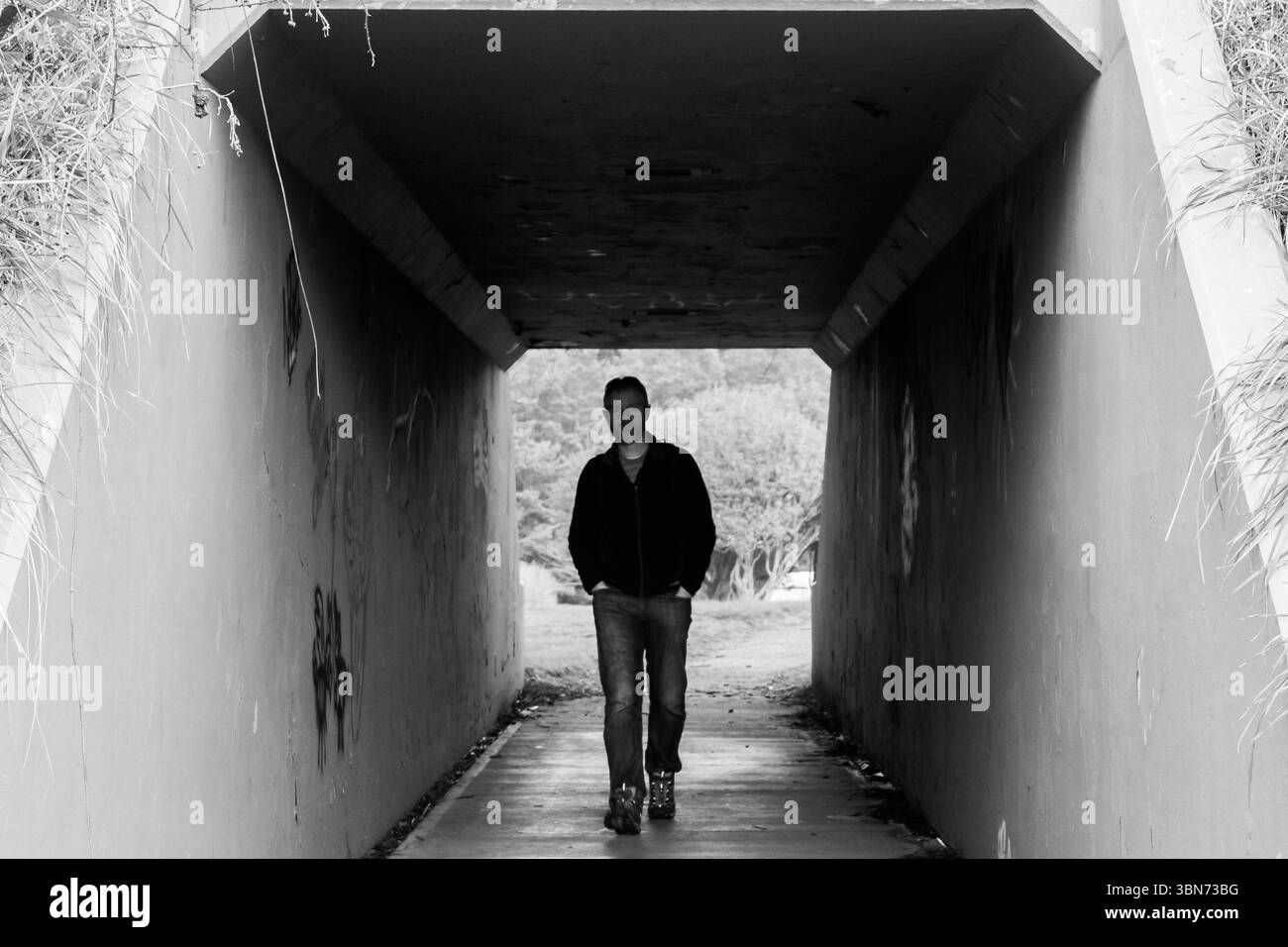 Yaquina Head, Oregon, USA - 27 febbraio 2017: Un uomo cammina attraverso un tunnel di cemento, le mani nelle tasche, verso la luce dall'altra parte Foto Stock