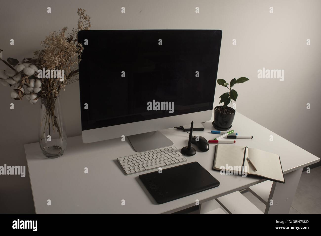 Spazio di lavoro minimalista per l'ufficio domestico con computer desktop, tastiera, notebook, tavoletta grafica, fiori secchi e una pianta su una scrivania bianca pulita. Lavora a casa Foto Stock