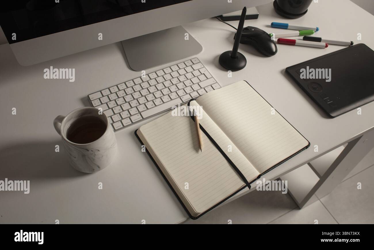 Spazio di lavoro minimalista per l'ufficio domestico con computer desktop, tastiera, notebook, tavoletta grafica, tazza con tè su una scrivania bianca pulita. Foto Stock