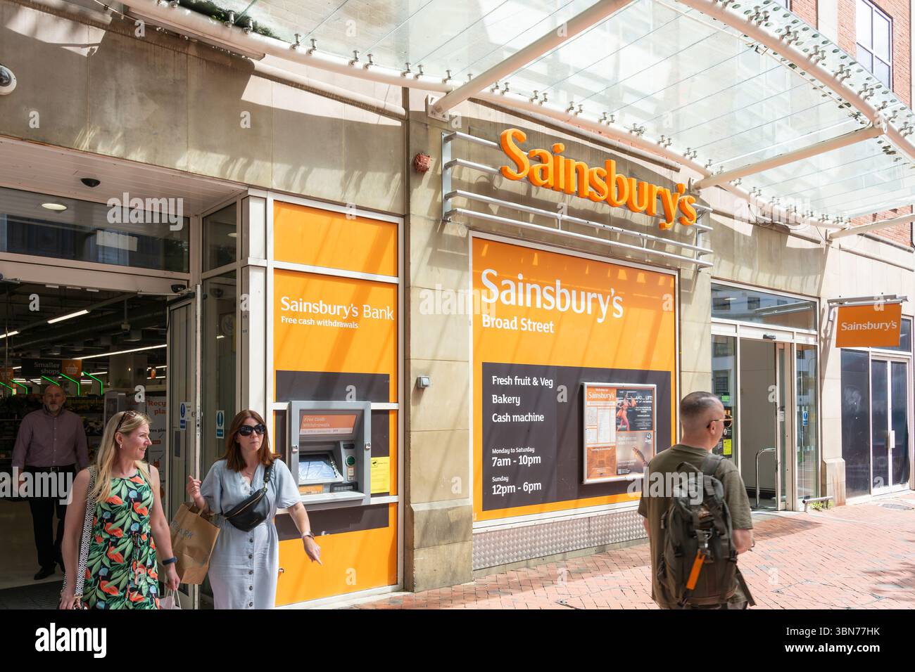 Gente che usciva dal supermercato di Sainsbury e passava davanti a un bancomat della Sainsbury's Bank in Broad Street a Reading, Regno Unito. Concetto: Rivenditore britannico Foto Stock