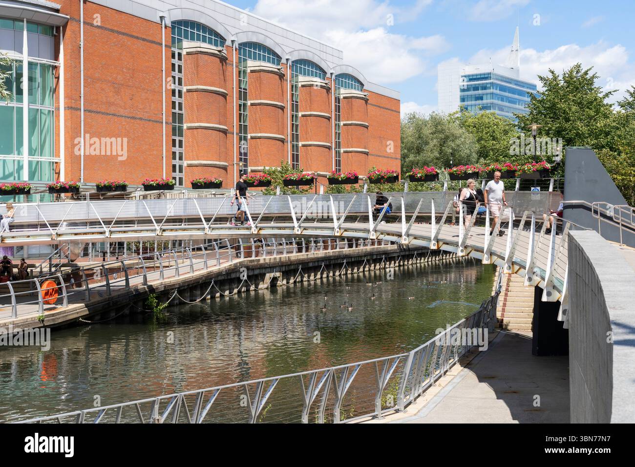 Persone che attraversano un ponte pedonale sul fiume Kennet fino all'Oracle Riverside, un'area pedonale con negozi e ristoranti. Reading, Regno Unito Foto Stock