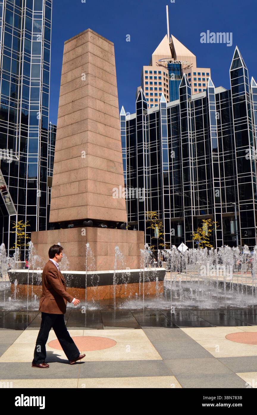 Un uomo adulto cammina intorno a una fontana e un obelisco, facendo esercizio durante la pausa pranzo al PPG Plaza di Pittsburgh. Foto Stock
