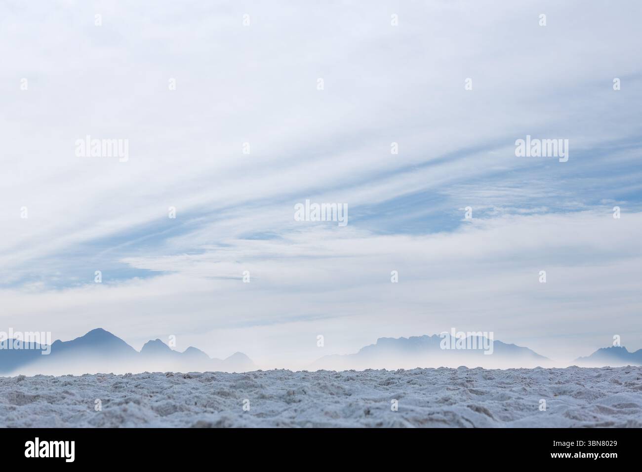 La superficie salina piatta si estende verso la cresta nebbiosa della montagna sotto strati di nuvole Foto Stock