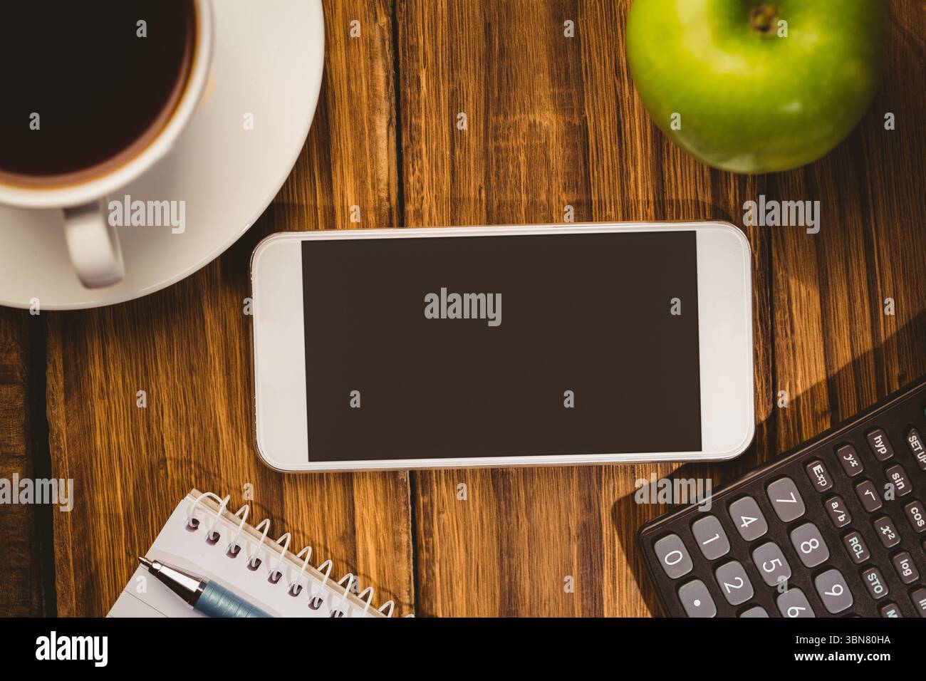 Lo smartphone si trova su una scrivania dal design piatto con tazza da caffè, piattino, mela, notebook, penna, calcolatrice Foto Stock