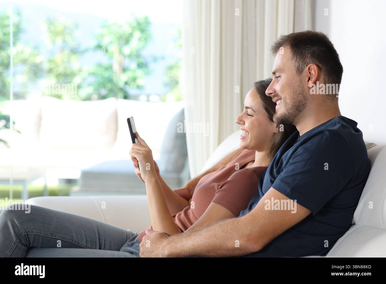 Profilo di una coppia felice che controlla il telefono cellulare insieme all'interno di una casa Foto Stock
