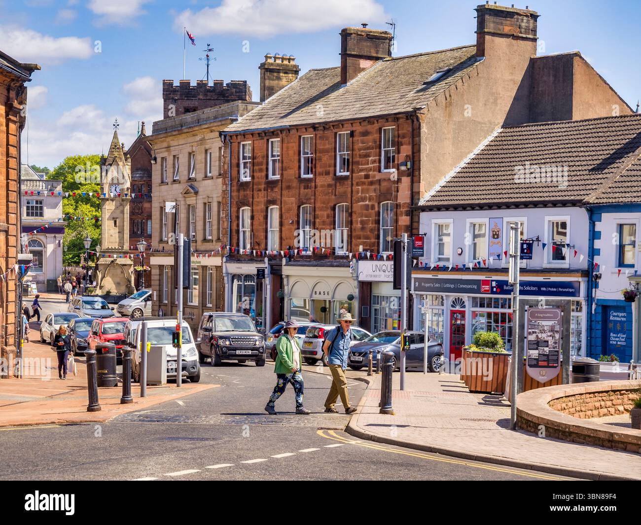 Mercato del mais, Penrith, Cumbria, Regno Unito - Una trafficata strada commerciale nel centro della città, con gente, traffico, sole e la torre dell'orologio, conosciuta anche come... Foto Stock