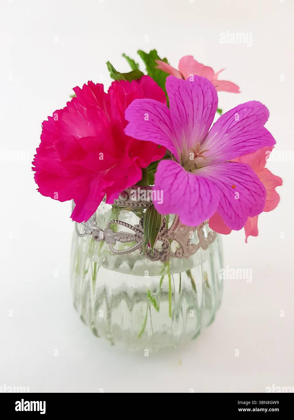 Un vaso decorativo in vetro con un'esposizione di fiori estivi colorati su sfondo bianco. Foto Stock