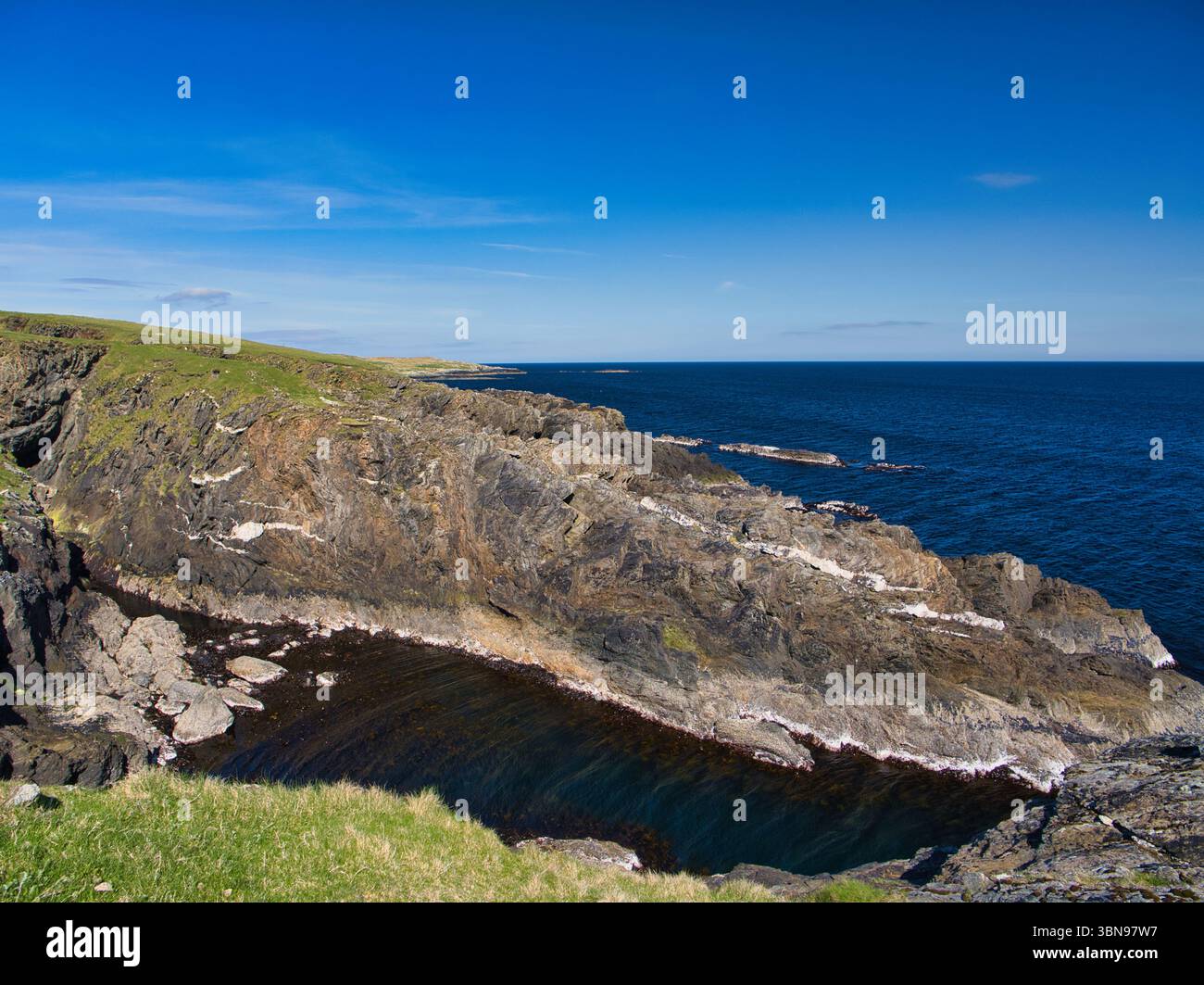 Scogliere scoscese con impressionanti strati di roccia bianca incontrano l'ampio mare di Ness of Ramnageo, Shetland, Regno Unito. Foto Stock
