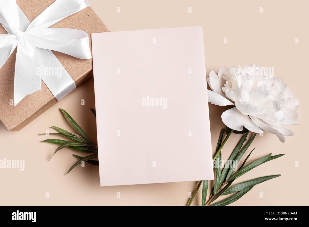 Mockup con biglietto d'auguri o invito, bianco vuoto con confezione regalo e decorazioni floreali su sfondo beige neutro, spazio per copie. Finta creativa ed elegante Foto Stock