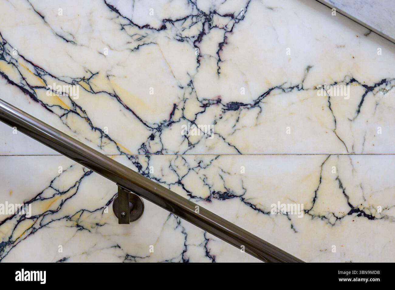 Un corrimano lucido corre lungo una parete di marmo bianco venato al vecchio municipio, mostrando intricati motivi scuri. Foto Stock
