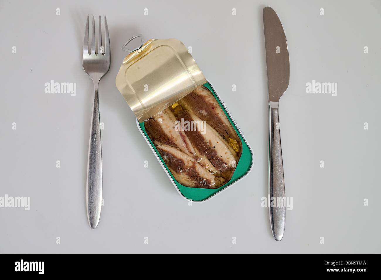 Barattolo metallico di sardine in olio su sfondo bianco con forchetta e coltello Foto Stock