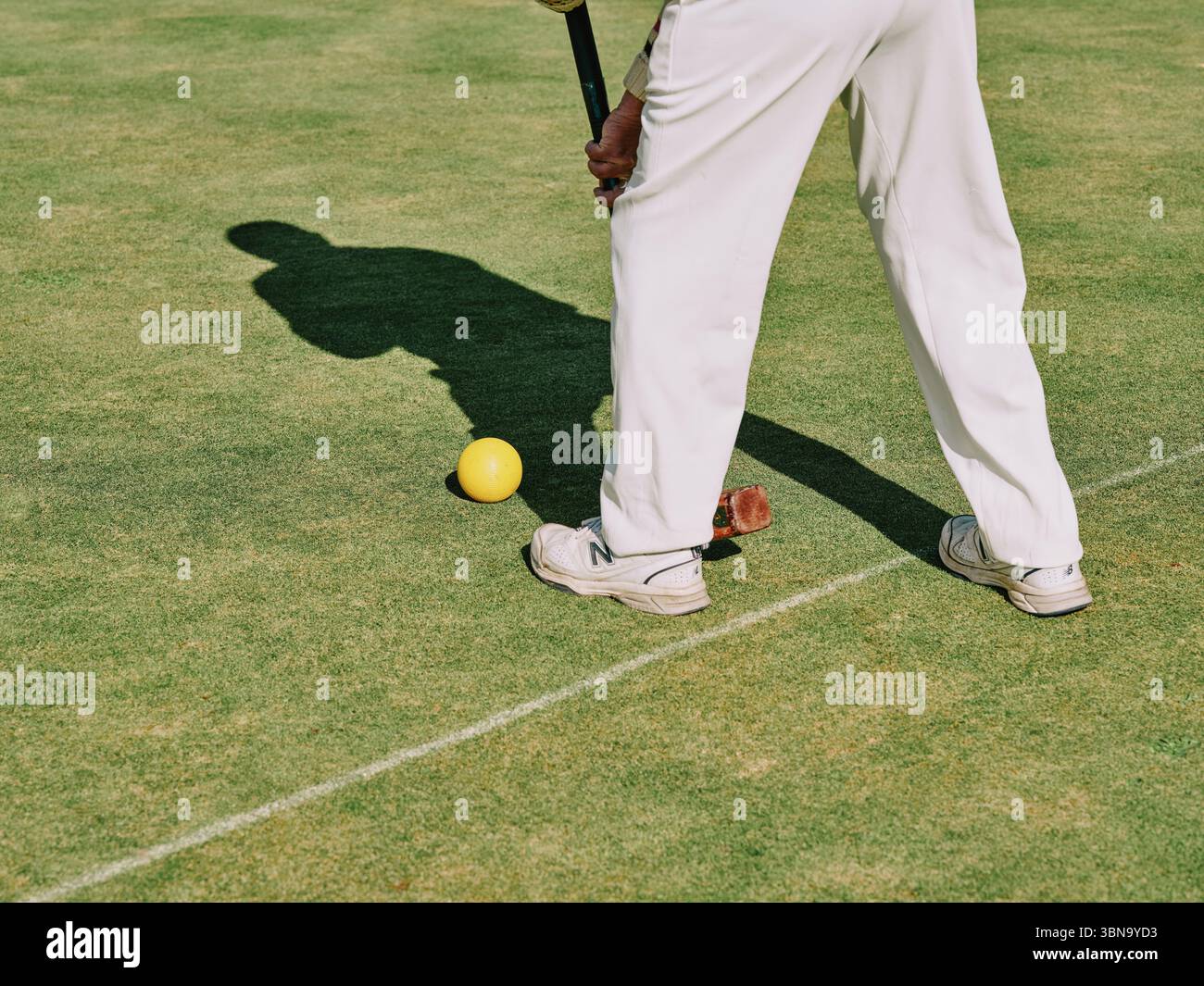 Un uomo vestito di bianchi tradizionali che gioca un croquet di prato tenendo un mazzetto di croquet circa per giocare un colpo in un giorno di estate. Foto Stock