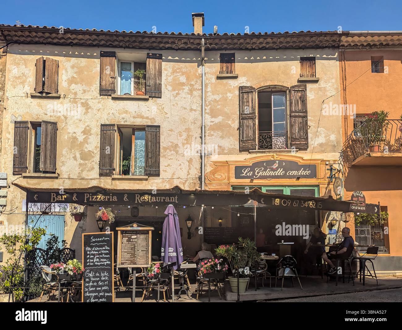Edifici tradizionali con Shutters e Un affascinante ristorante con posti a sedere all'aperto nel tipico villaggio provenzale di Saint-Saturnin-lès-Apt, provenzale Foto Stock