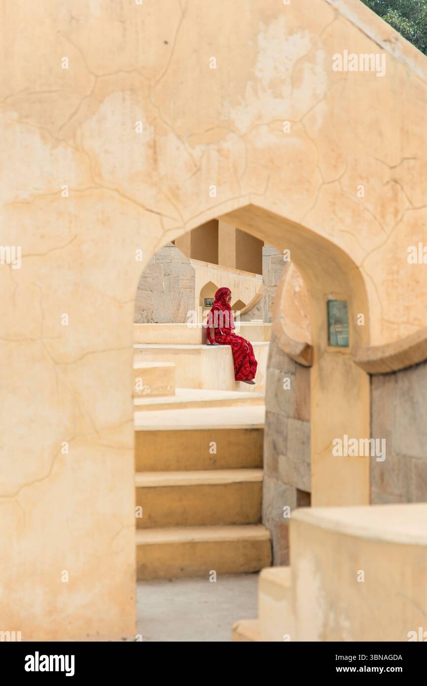 Una donna indiana che indossa un sari rosso è seduta a Jantar Mantar, Jaipur, uno storico osservatorio astronomico costruito dal Maharaja Jai Singh II Foto Stock