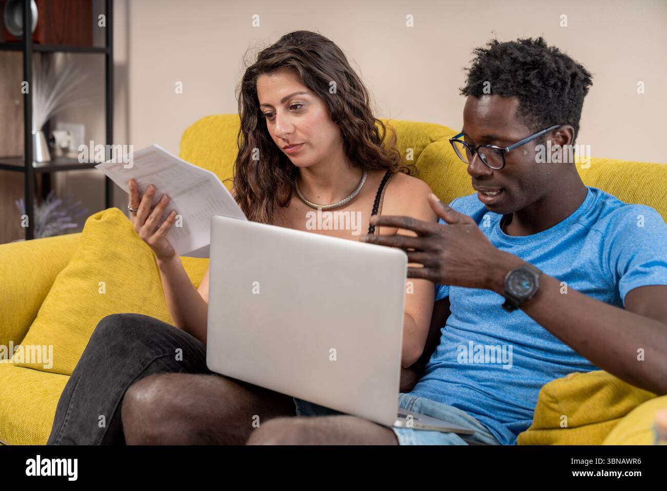 Un giovane spiega i documenti finanziari al suo partner mentre gestiscono il loro budget insieme a casa con un notebook. Foto Stock