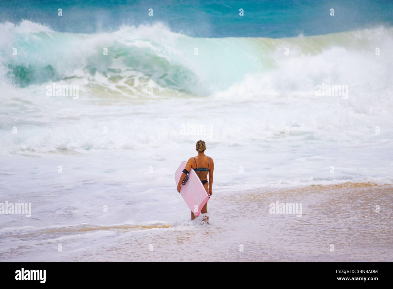 Bodyboarder entra in una potente tavola rosa in mano su una spiaggia tropicale. Avventura nell'oceano, stile di vita in spiaggia e energia senza paura catturate Foto Stock