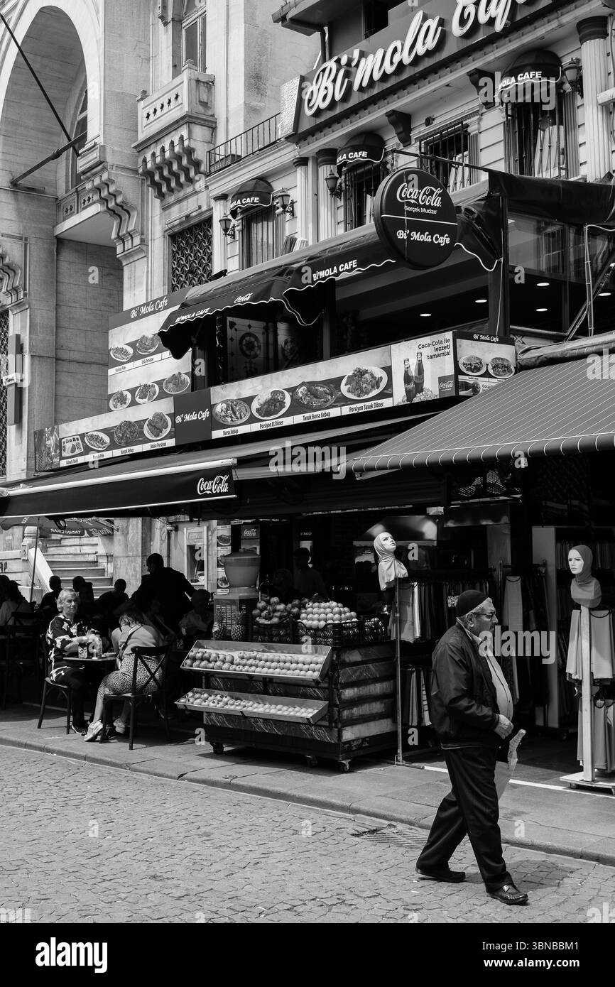 La folla si riunisce in caffetterie e negozi all'aperto a Istanbul, dove i venditori vendono frutta mentre i pedoni passeggiano, creando un'atmosfera urbana vivace. Foto Stock