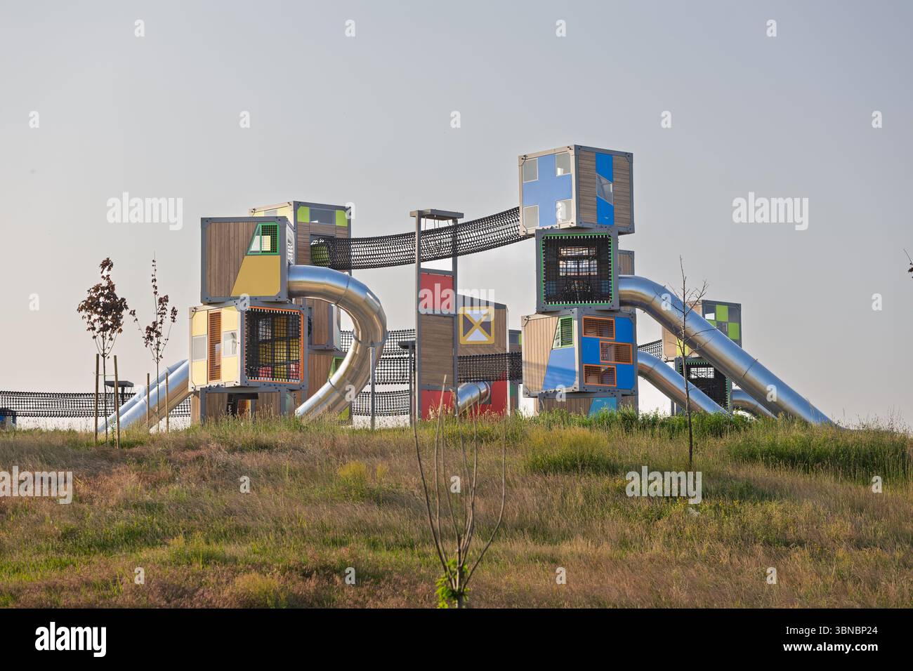 Un moderno parco giochi presenta torri vibranti collegate da ponti e scivoli, che promuovono divertimento e avventura all'aperto. Circondato da erba e cieli aperti, Foto Stock