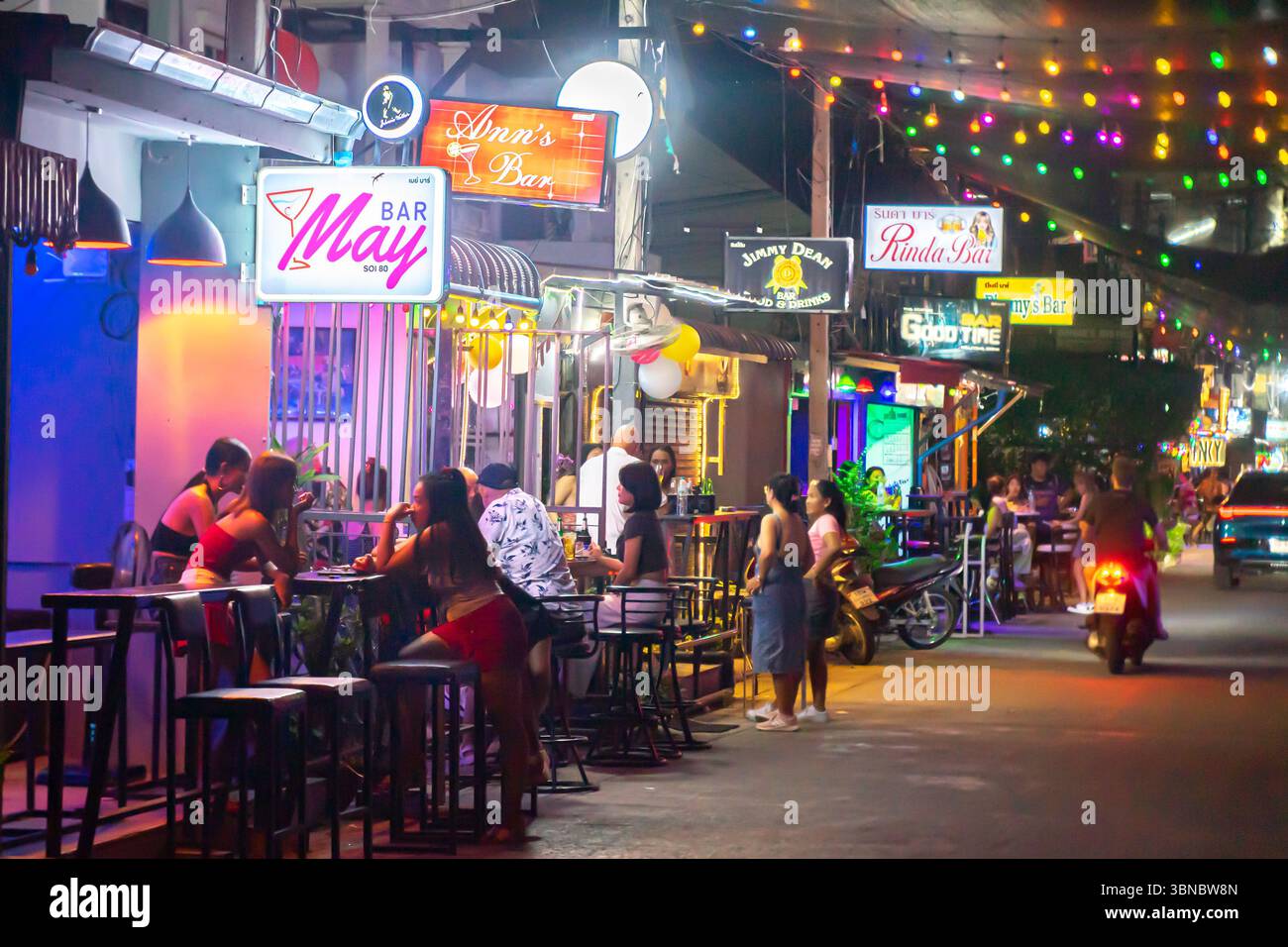 Scena di strada di notte con bar, posti a sedere all'aperto, donne, sotto vari cartelli al neon, Hua Hin, Thailandia Foto Stock