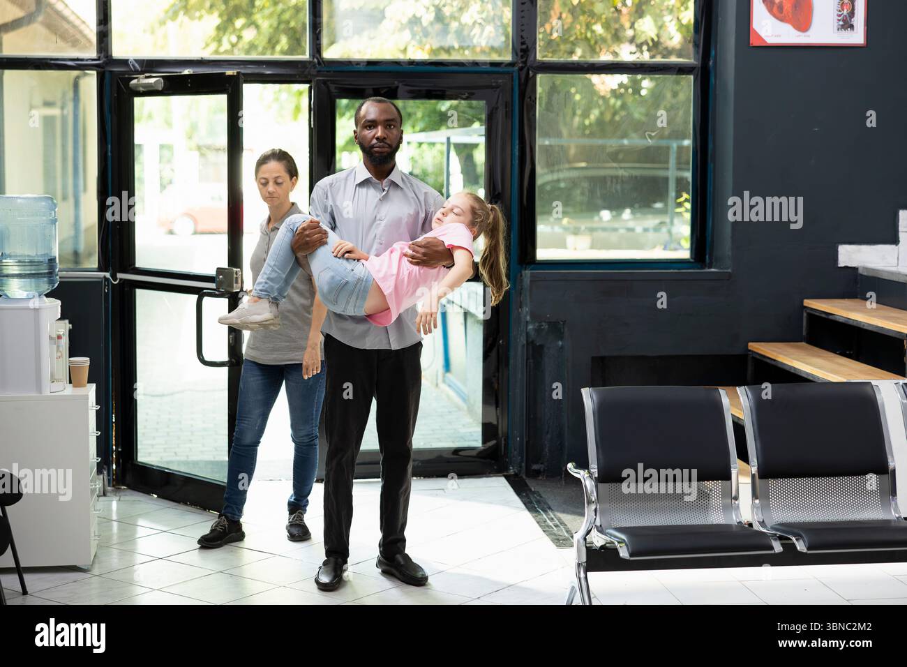 Ragazza svenuta e suo padre afroamericano la sta portando in ospedale, in attesa di risposta immediata da parte dell'equipe medica. Situazione clinica caratterizzata da urgenza e preoccupazione familiare. Foto Stock