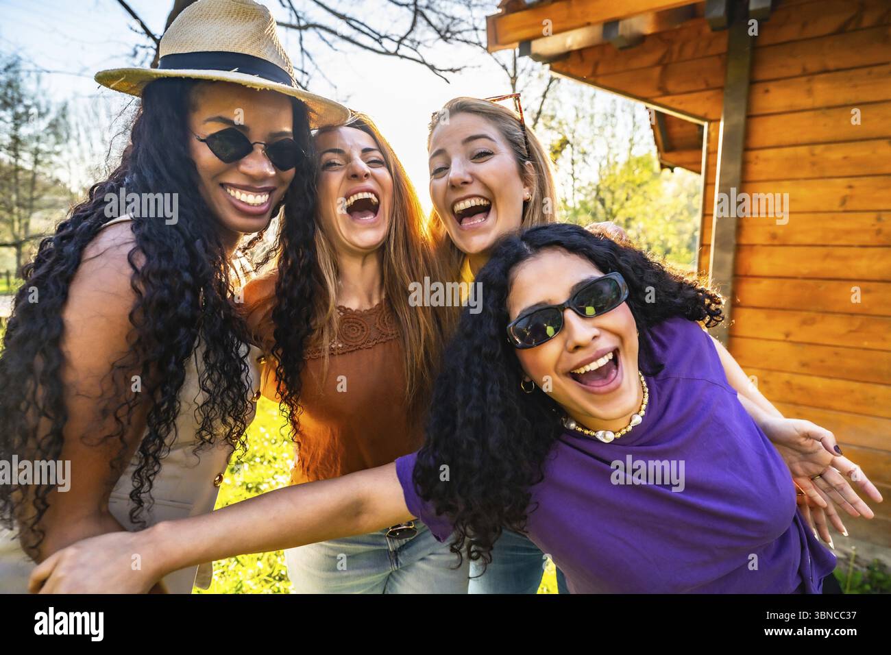Quattro amiche multietniche si divertono insieme in un parco, ridendo e godendosi la compagnia reciproca Foto Stock