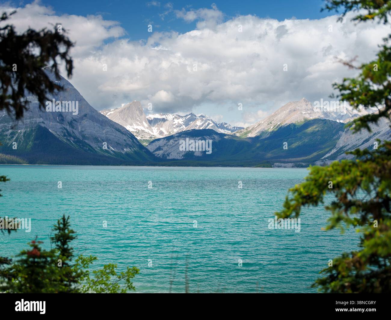 Lago glaciale turchese circondato da montagne innevate e alberi sempreverdi in Alberta, Canada. Splendido paesaggio naturale con nuvole spettacolari Foto Stock