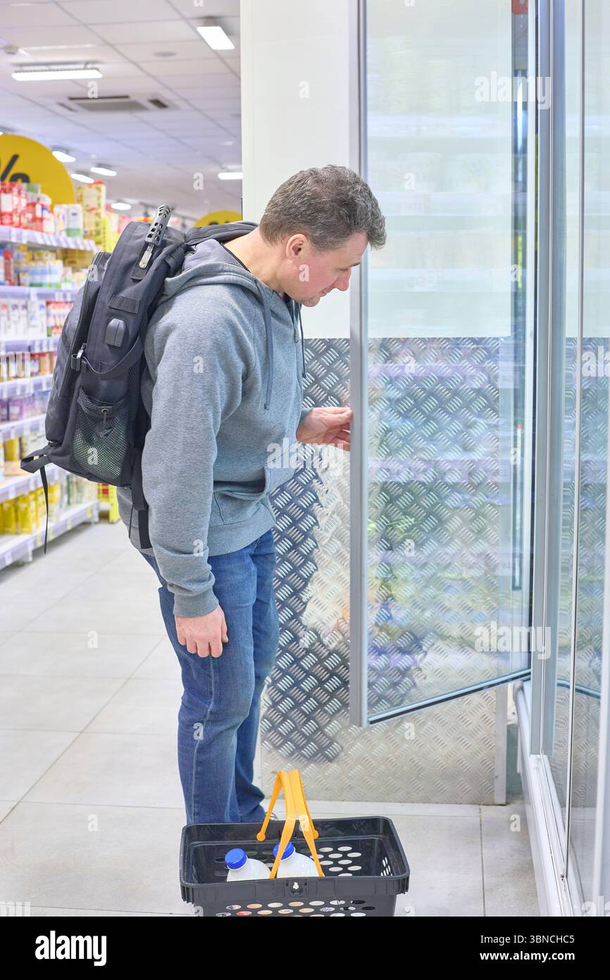 La vita di tutti i giorni si svolge quando un uomo con uno zaino esamina gli articoli in un negozio di alimentari, perfetto per illustrare concetti come le scelte dei consumatori, lo shopping ha Foto Stock