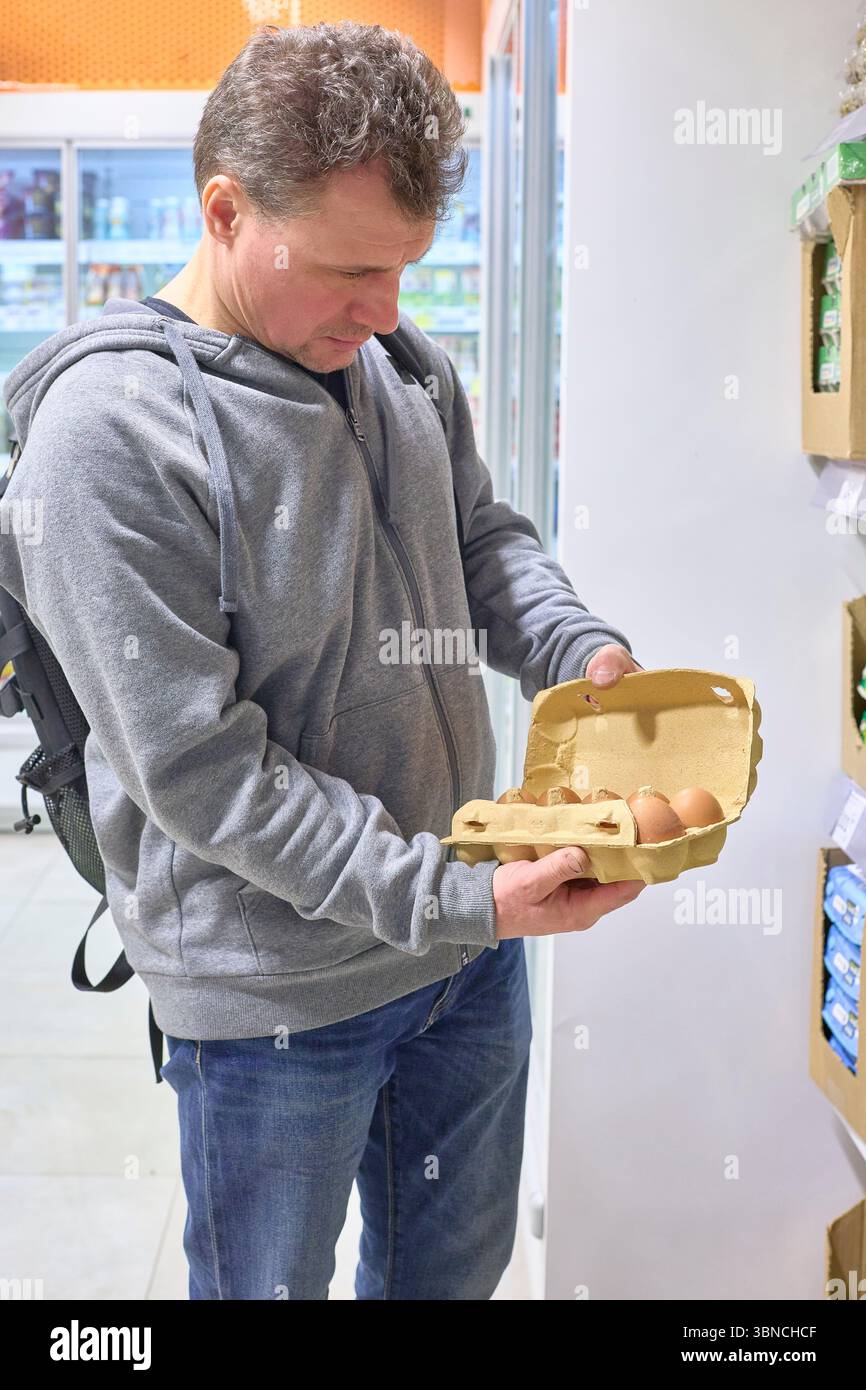 La contemplazione riempie lo sguardo degli acquirenti, ispezionando attentamente le uova fresche in un vivace supermercato, una scena di vita quotidiana, scelta e mentalità Foto Stock