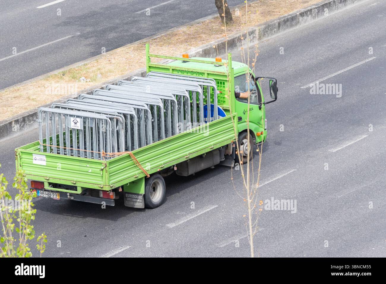 Autocarro a pianale verde che trasporta barriere metalliche sovrapposte per il controllo della folla che guida in autostrada, fornendo attrezzature per la gestione degli eventi Foto Stock