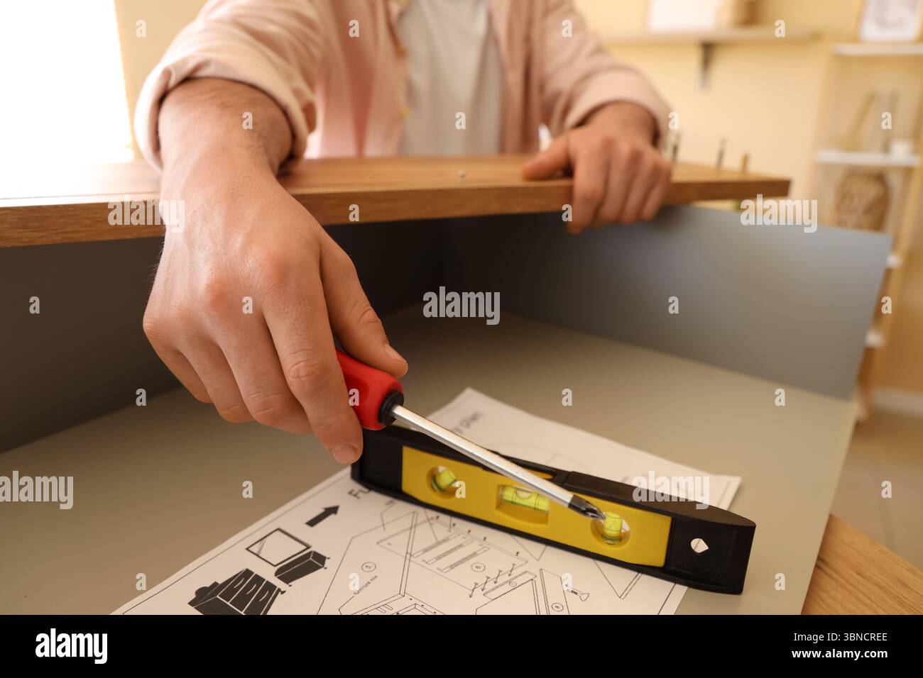 Uomo con cacciavite e livella che assembla cassettiera a casa, primo piano Foto Stock