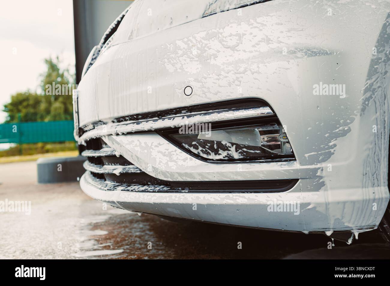 Vista ravvicinata di un'auto color argento ricoperta di bolle di sapone durante un autolavaggio, evidenziando l'importanza della pulizia e della cura del veicolo per la manutenzione Foto Stock