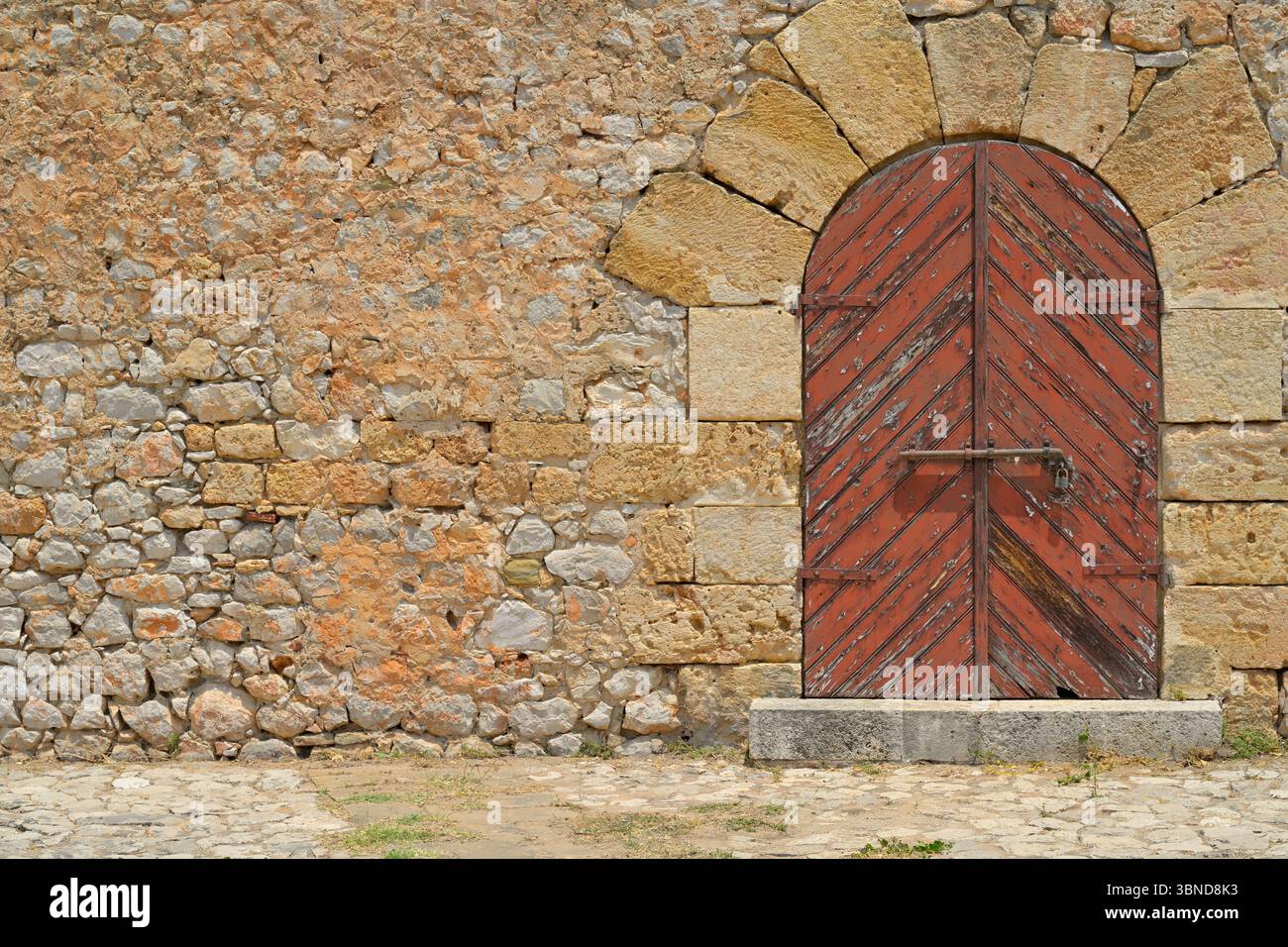 La vecchia porta d'ingresso nel muro di pietra di una storica ex prigione necessita di qualche ristrutturazione. Peloponneso, Grecia. Copia spazio per il testo. Foto Stock