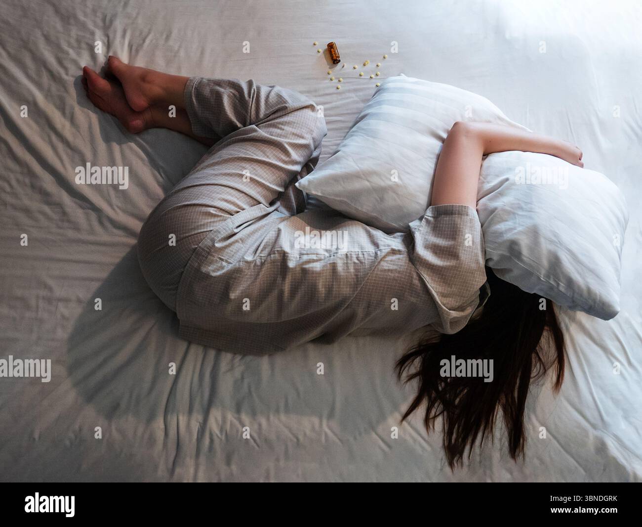 donna sdraiata sul letto, coprirsi la testa con un cuscino soffre di insonnia, sonniferi accanto a lei sul letto. sopra la vista della donna si arriccia nello stress Foto Stock