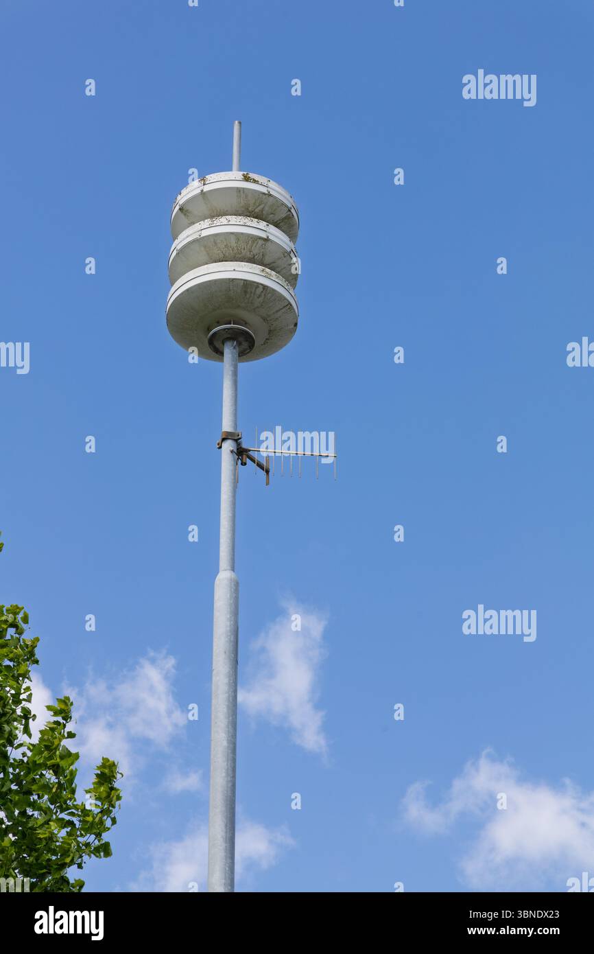 Una sirena e un'antenna di difesa civile moderna si stagliano contro un cielo azzurro limpido con nuvole sparse, pronti ad avvisare la comunità. Foto Stock