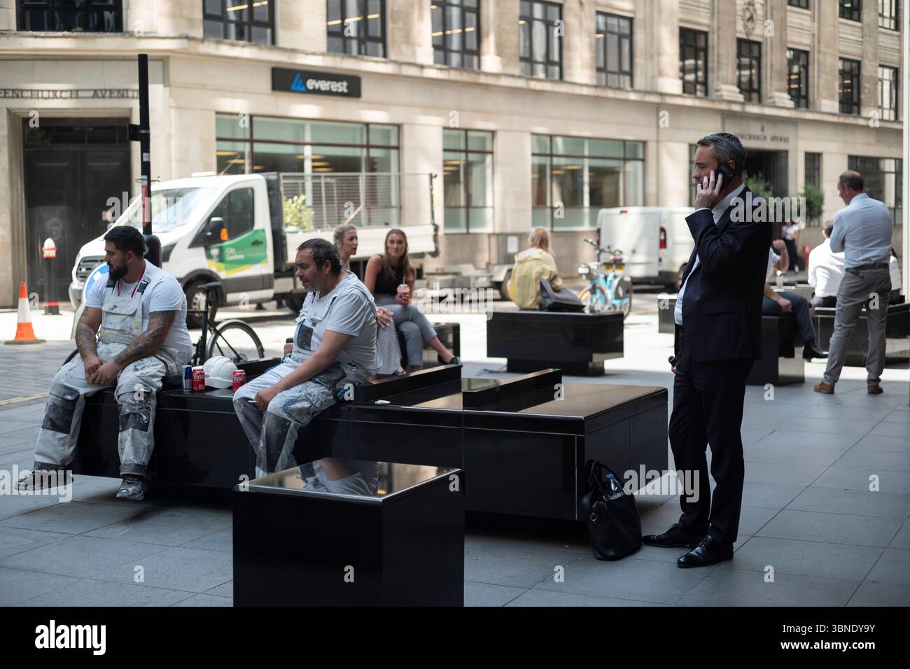 Il lavoratore di città risponde a una chiamata sul suo smartphone accanto ai lavoratori manuali nel cuore del quartiere finanziario, City of London, Inghilterra, Regno Unito Foto Stock