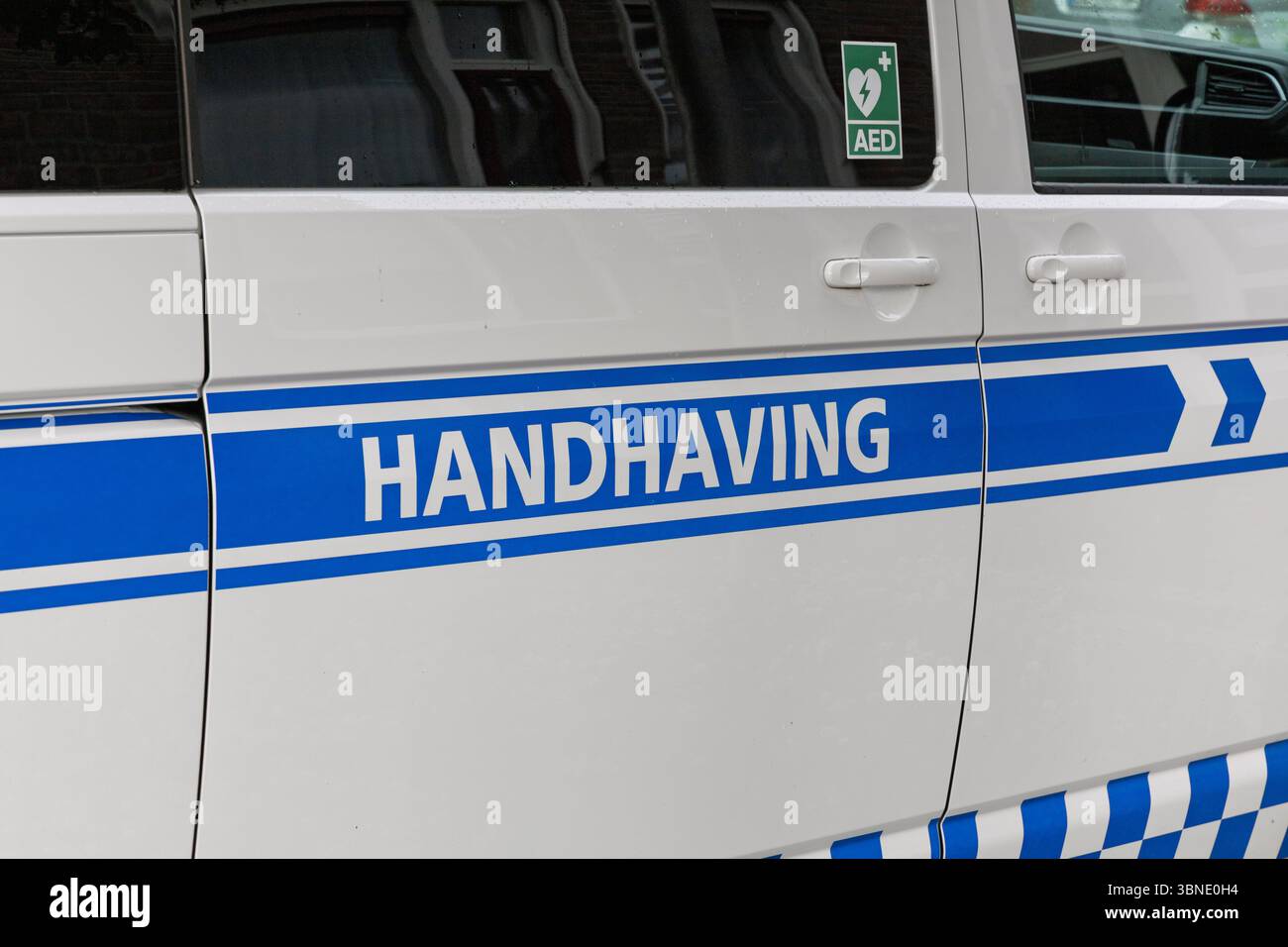 Primo piano di un veicolo bianco con "HANDHAVING" (Enforcement) in blu e simbolo di AED che indica la pubblica sicurezza e i servizi di emergenza. Amsterdam, ne Foto Stock