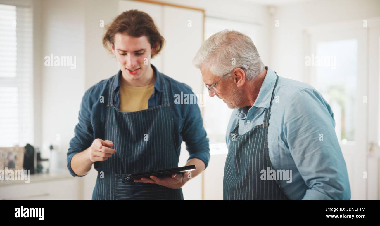 Uomini, chef e grembiule con tablet in cucina casalinga per l'ospitalità o l'abilità culinaria in cucina. Maturo, mentore o persona con aiuto, tecnologia o. Foto Stock