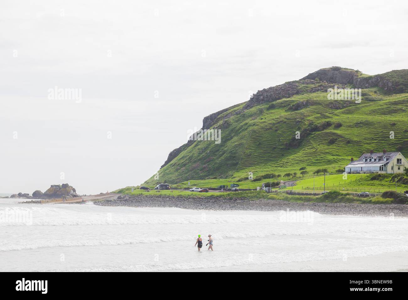 Surfisti e nuotatori sulla spiaggia di Carnlough on the Co Antrim Coast, Irlanda del Nord. Uno dei percorsi costieri più belli d'Irlanda. Foto Stock