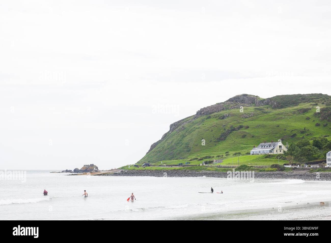 Surfisti e nuotatori sulla spiaggia di Carnlough on the Co Antrim Coast, Irlanda del Nord. Uno dei percorsi costieri più belli d'Irlanda. Foto Stock