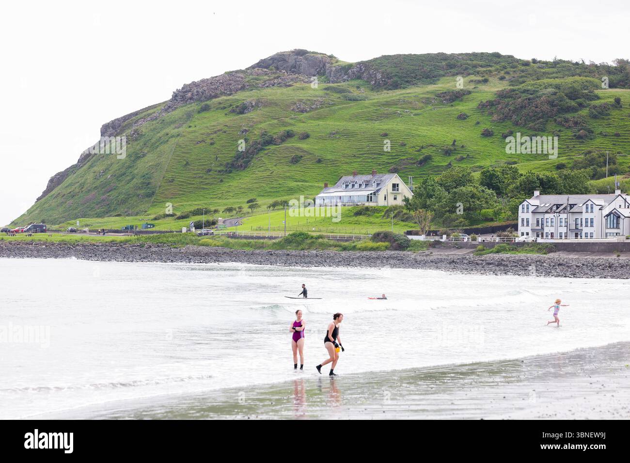 Surfisti e nuotatori sulla spiaggia di Carnlough on the Co Antrim Coast, Irlanda del Nord. Uno dei percorsi costieri più belli d'Irlanda. Foto Stock