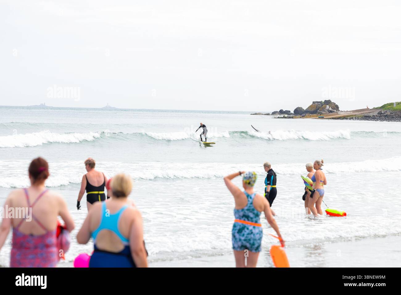 Surfisti e nuotatori sulla spiaggia di Carnlough on the Co Antrim Coast, Irlanda del Nord. Uno dei percorsi costieri più belli d'Irlanda. Foto Stock