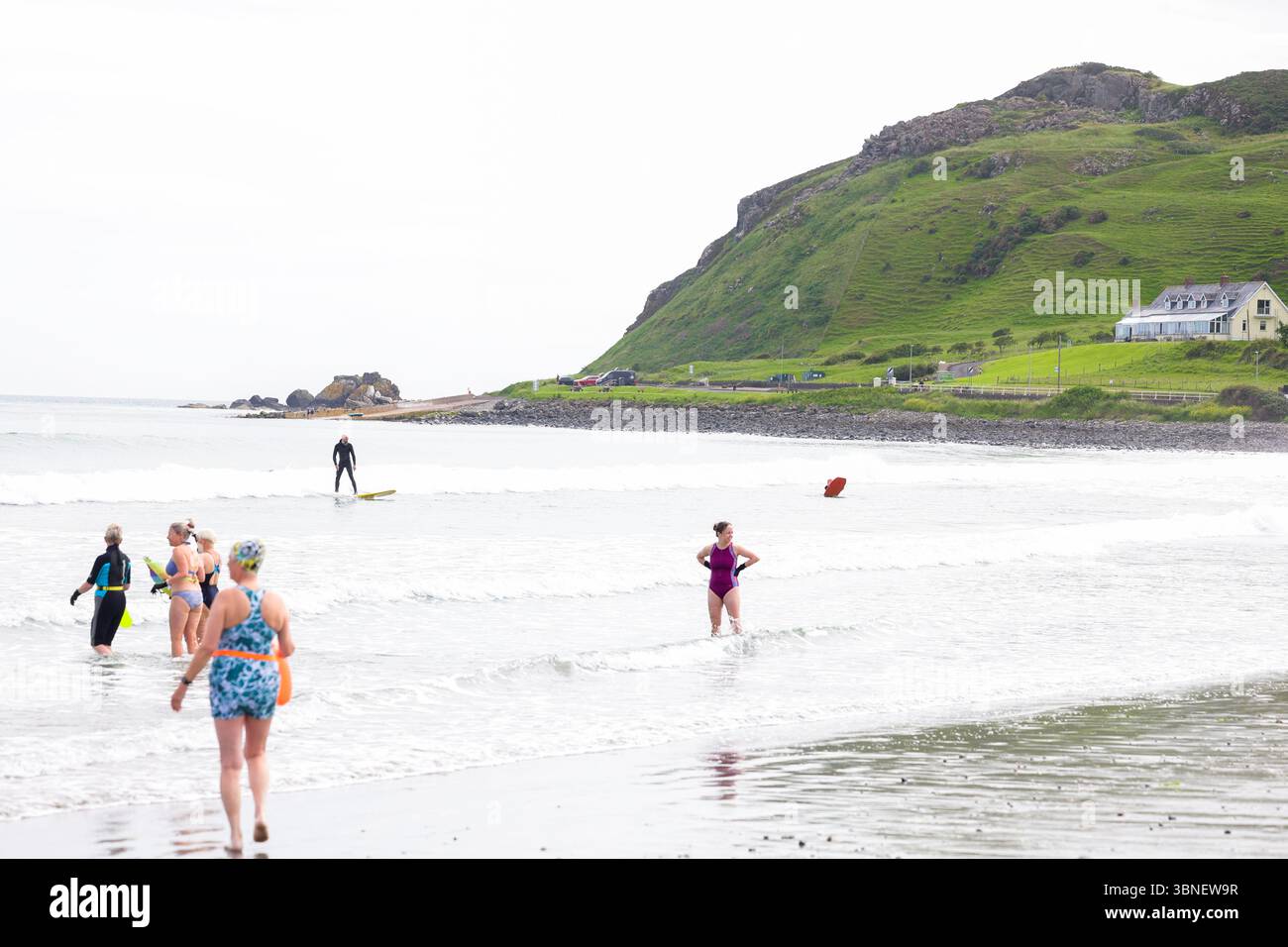 Surfisti e nuotatori sulla spiaggia di Carnlough on the Co Antrim Coast, Irlanda del Nord. Uno dei percorsi costieri più belli d'Irlanda. Foto Stock