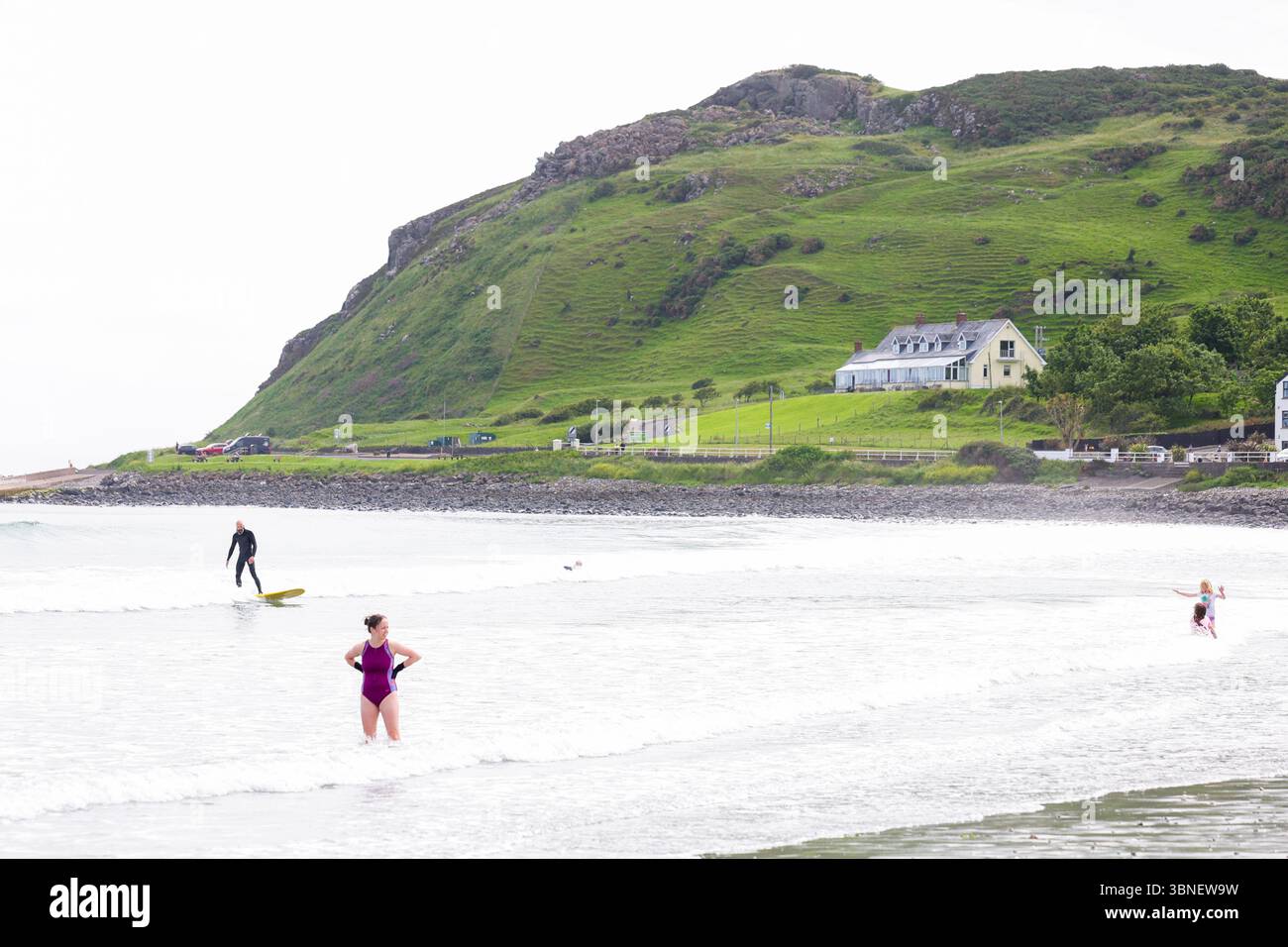 Surfisti e nuotatori sulla spiaggia di Carnlough on the Co Antrim Coast, Irlanda del Nord. Uno dei percorsi costieri più belli d'Irlanda. Foto Stock