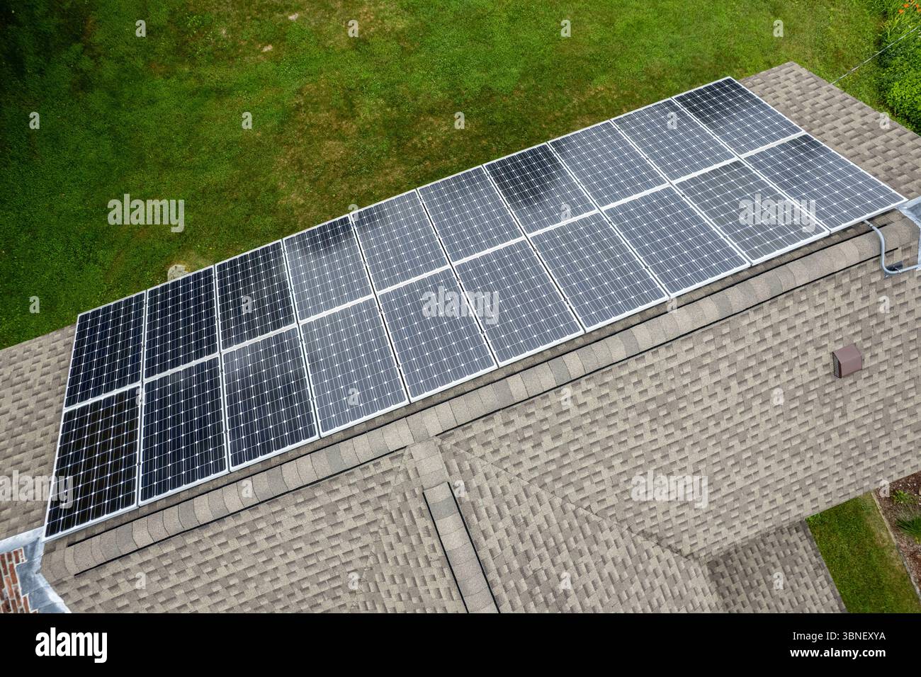 Angolo ravvicinato che mostra i moderni pannelli solari installati su un tetto in tegole di asfalto con sfondo alberato. Foto Stock