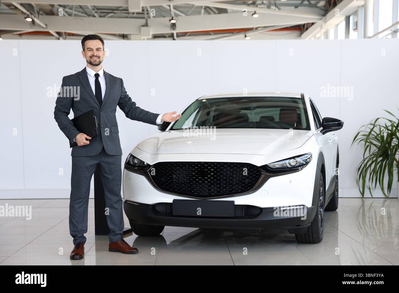 Venditore sorridente con appunti che mostra la nuova auto in salone Foto Stock