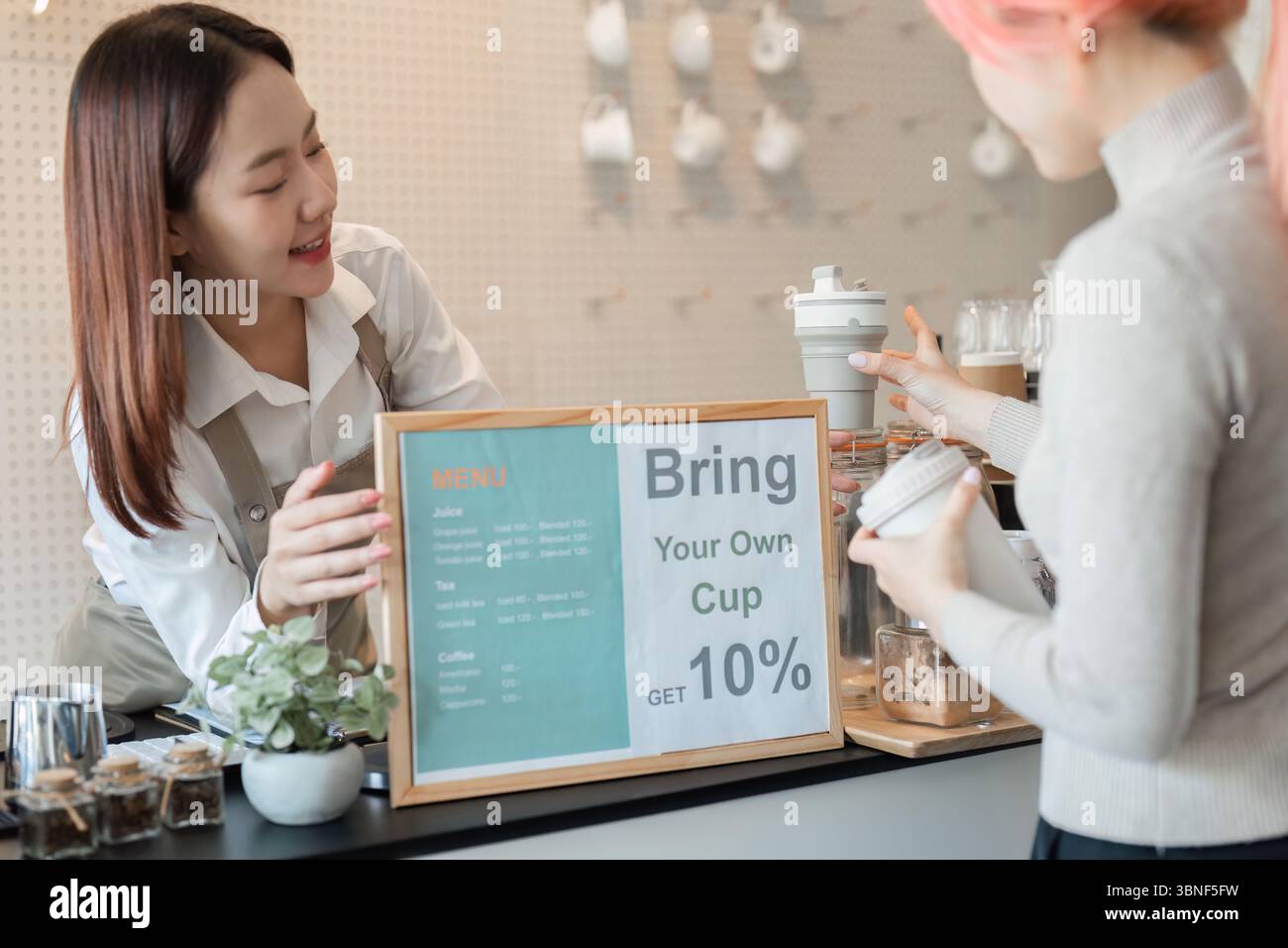 Sostenibilità e cultura del caffè. Un barista che incoraggia i clienti a portare tazze riutilizzabili a prezzo scontato. Foto Stock